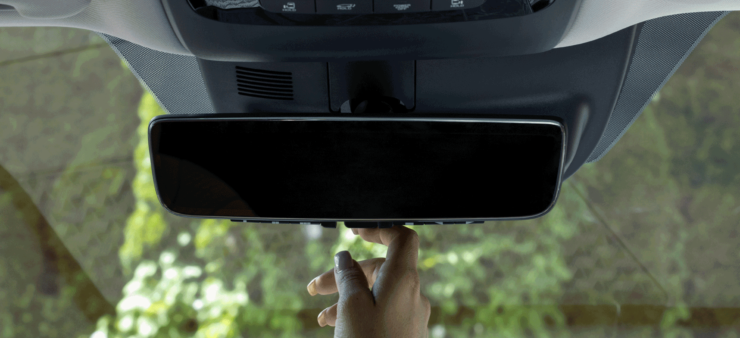 Kia vehicle interior, zoomed in view of the digital display rearview mirror showing trees and bushes in the screen