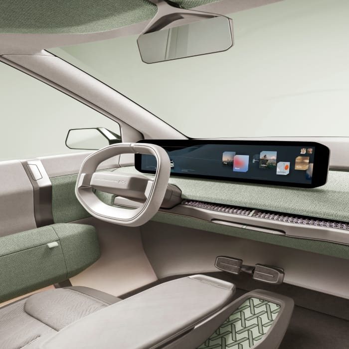 Kia EV3 concept vehicle interior, driver's seat view, featuring a panoramic digital screen and light green interior accents.