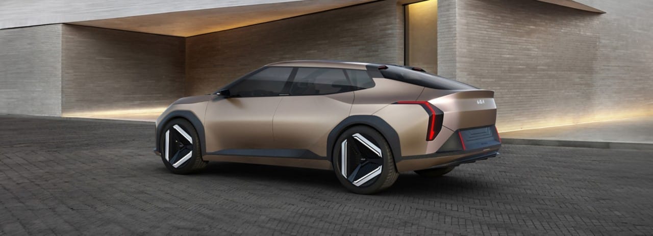 Prototipo del Kia EV4 en dorado champán, vista trasera de tres cuartos, estacionado delante de una casa moderna