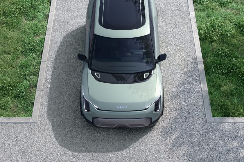 Prototipo del Kia EV3 en verde a vista de pájaro con techo corredizo panorámico, estacionado en una carretera asfaltada rodeada de hierba.