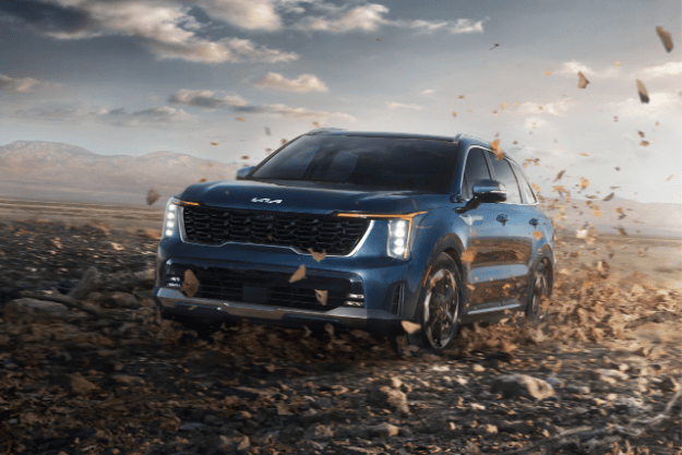 2025 Kia Sorento Hybrid in blue, side view, driving on a dirt road with LED headlights on