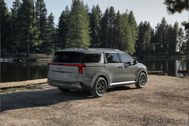2025 Kia Carnival parked off-road looking over a lake, rear three-quarter view