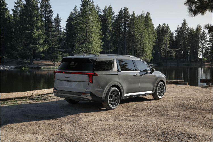 2025 Kia Carnival parked off-road looking over a lake, rear three-quarter view